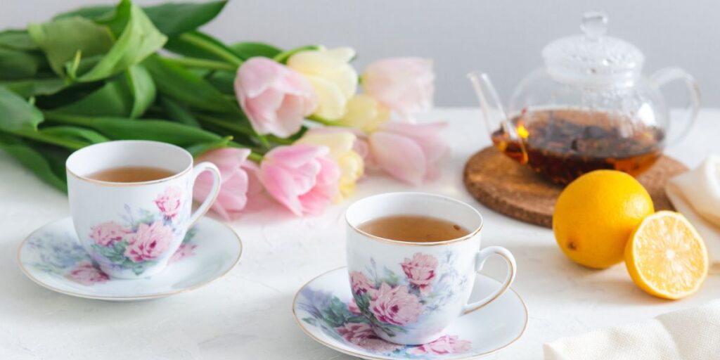 Two tea cups, lemon, tea pot, and tulips on table