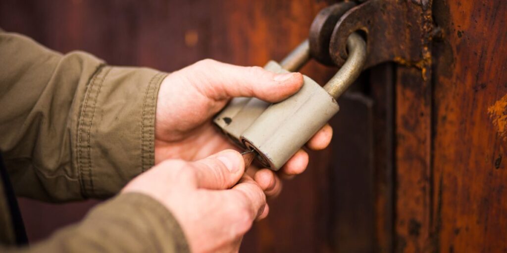 Man's hands close the lock, unlocking an old padlock